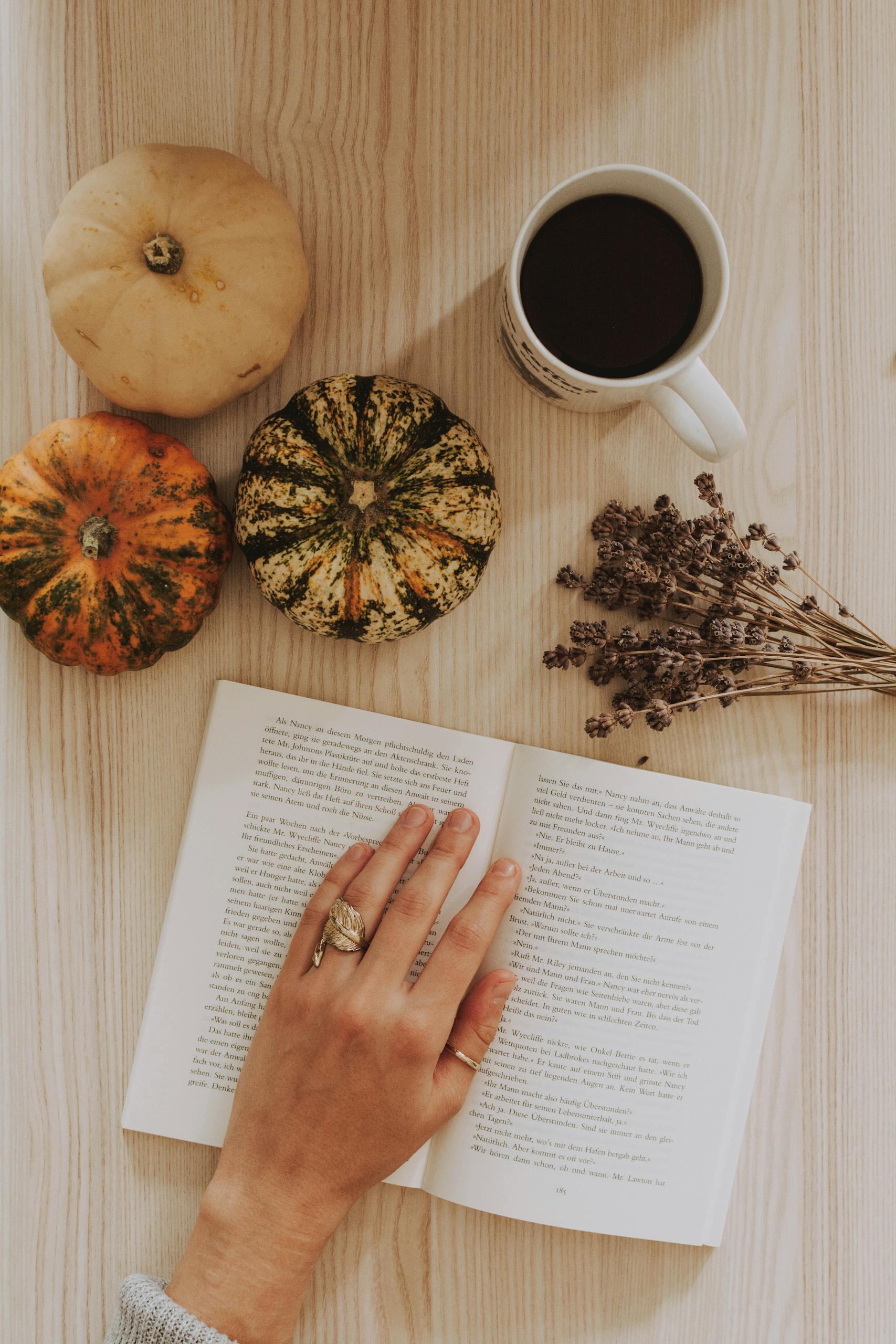 Cozy autumn scene of a hand reading, surrounded by pumpkins, coffee, and dried herbs.